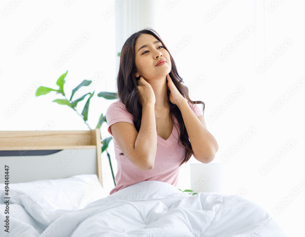 Asian young beautiful happy sleepy female teenager in casual pajama outfit waking up fresh in morning sitting smiling closed eyes under white blanket on bed in bedroom massaging stretching neck Asian young beautiful happy sleepy female teenager in casual pajama outfit waking up fresh in morning sitting smiling closed eyes under white blanket on bed in bedroom massaging stretching neck