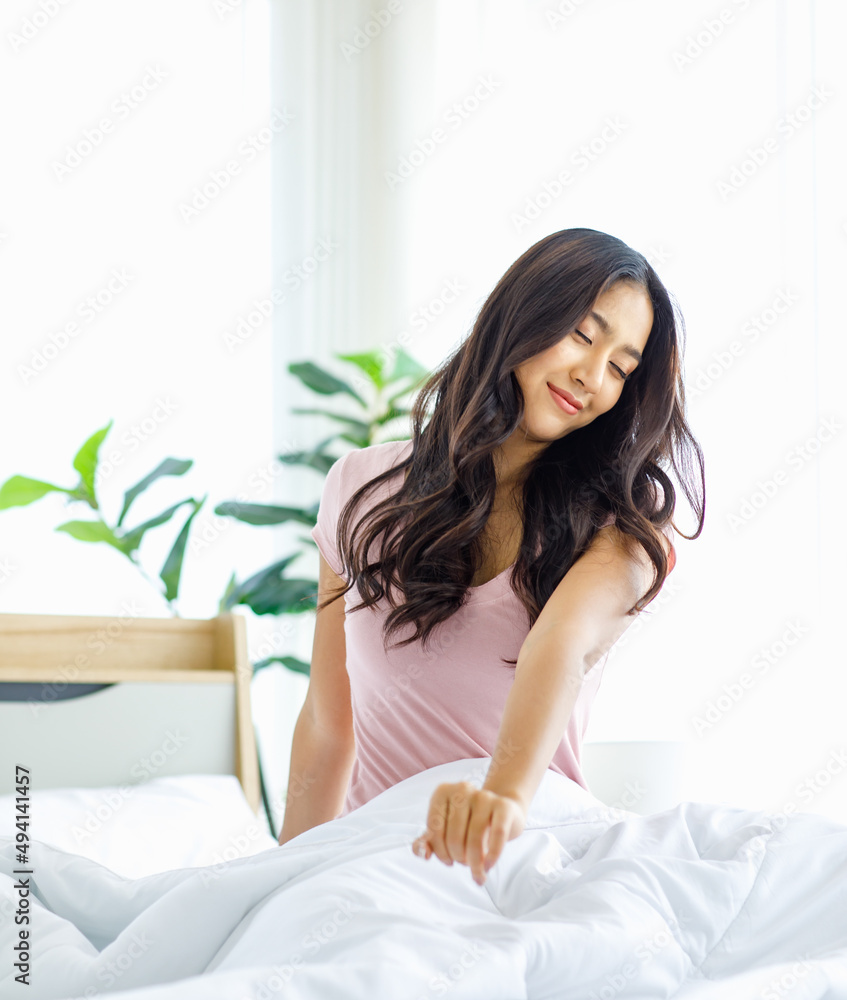 Asian young beautiful happy lazy sleepy female teenager model in casual pajama outfit waking up fresh in morning sitting alone smiling under white blanket on bed in bedroom stretching relaxing arms Asian young beautiful happy lazy sleepy female teenager model in casual pajama outfit waking up fresh in morning sitting alone smiling under white blanket on bed in bedroom stretching relaxing arms