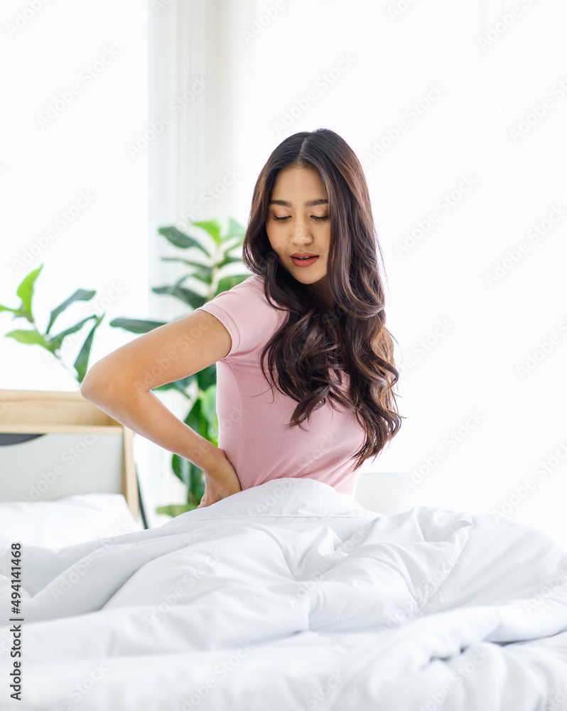 Asian young beautiful happy sleepy female teenager in casual pajama outfit waking up fresh in morning sitting smiling closed eyes under white blanket on bed in bedroom massaging stretching neck Asian young beautiful happy sleepy female teenager in casual pajama outfit waking up fresh in morning sitting smiling closed eyes under white blanket on bed in bedroom massaging stretching neck