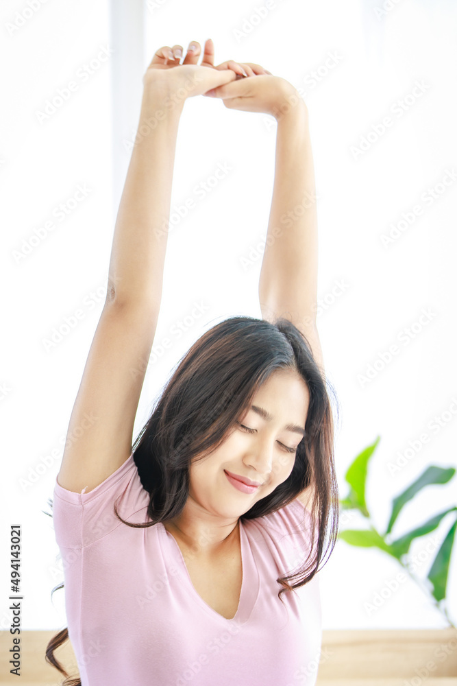 Asian young beautiful female model in casual pajama waking up fresh sitting under white clean blanket in weekend vacation morning on bed in hotel bedroom holding arms and hands up stretching smiling Asian young beautiful female model in casual pajama waking up fresh sitting under white clean blanket in weekend vacation morning on bed in hotel bedroom holding arms and hands up stretching smiling