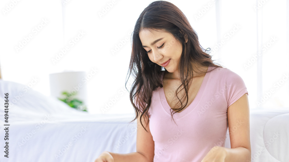 Asian young pretty female teenager traveler in casual outfit sitting smiling near bed in bedroom holding looking at sunglasses while preparing packing clothes in trolley luggage for holiday vacation Asian young pretty female teenager traveler in casual outfit sitting smiling near bed in bedroom holding looking at sunglasses while preparing packing clothes in trolley luggage for holiday vacation