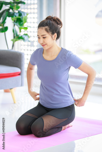 Asian young happy peaceful calm healthy female model in casual sporty outfit smiling doing yoga stretching exercise on mat learning studying online pilates class via laptop computer in living room