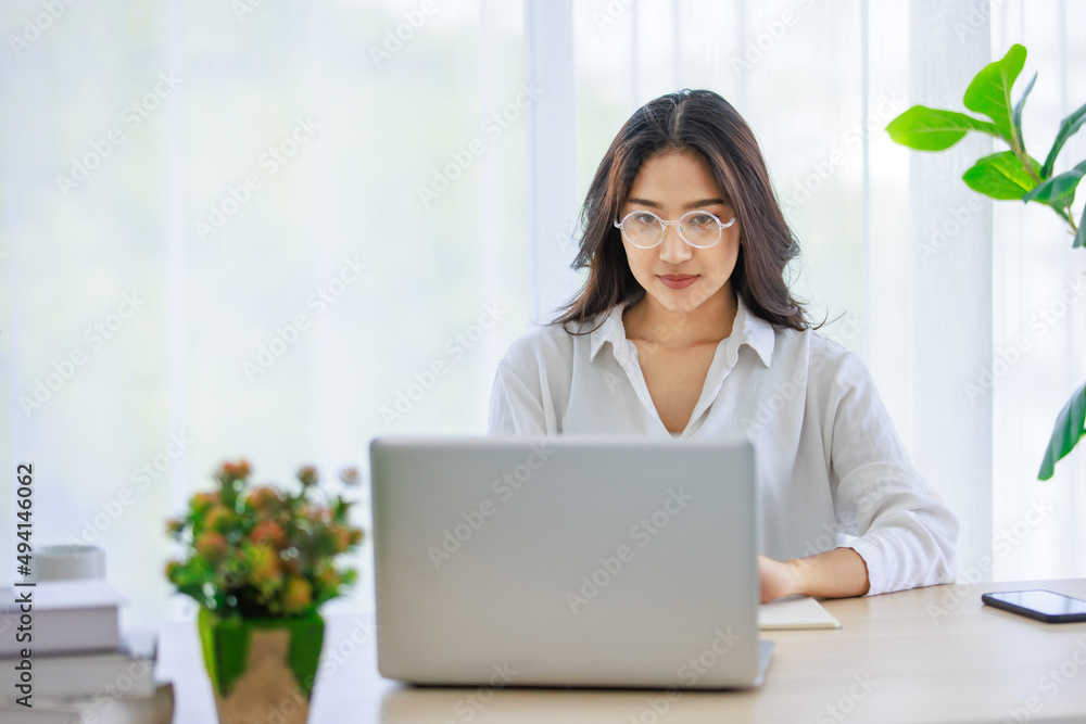 Asian young beautiful female university student wearing optical eyeglasses sitting at working desk remotely studying learning streaming online via laptop notebook computer at home during quarantine Asian young beautiful female university student wearing optical eyeglasses sitting at working desk remotely studying learning streaming online via laptop notebook computer at home during quarantine