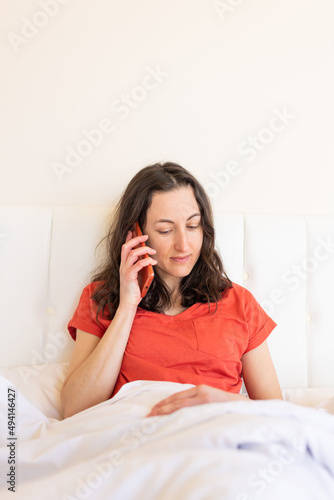 A woman sits on a bed and calling on the phone