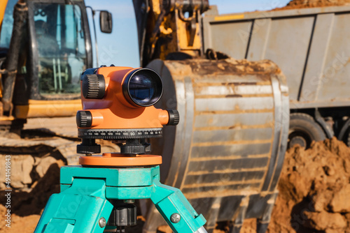 Level with an excavator in the background. Construction level or theodolite. Geodetic instruments and equipment for the construction and earthworks.