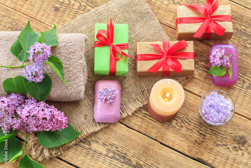 Towels, soap, gifts, candle and lilac flowers on wooden background.