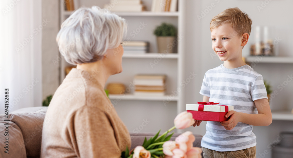 Cheerful little boy giving present to grandmother