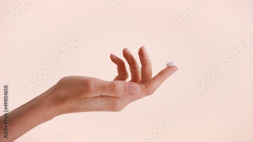 Close-up shot of a female hand with a drop of beauty cream on the top of the finger against beige background photo