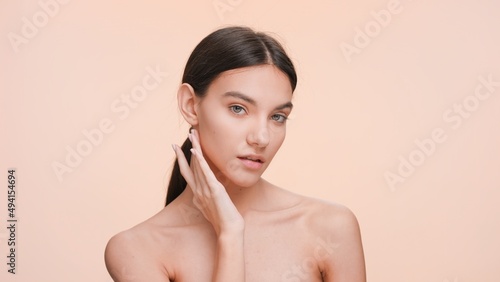Medium close-up beauty portrait of Young slim woman who gently touches her jawline and looks at the camera | Beauty and skin care concept