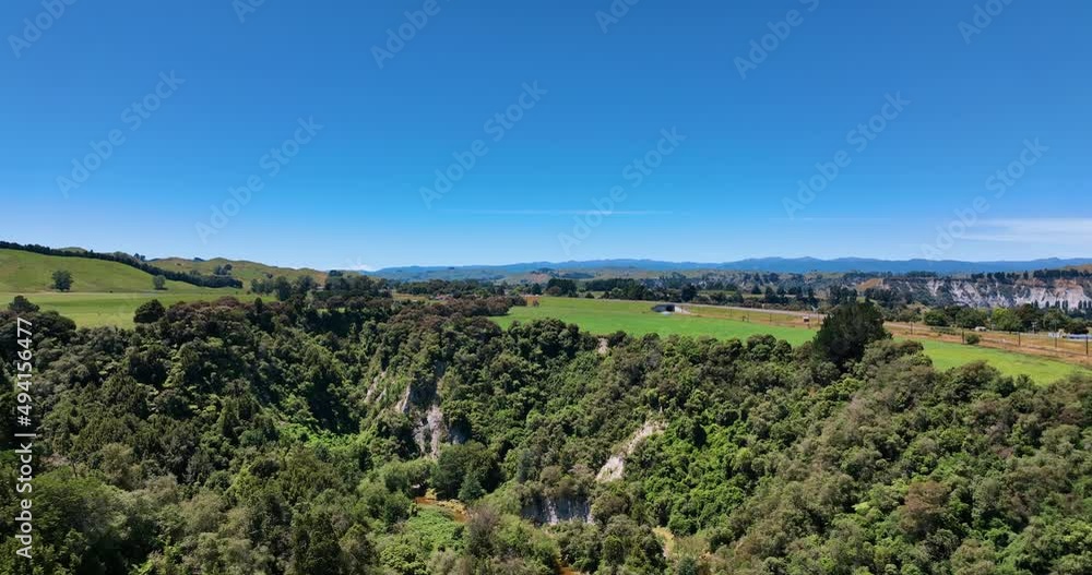 Aerial exposes steep bush-clad gorge surrounded by flat green fields - NZ