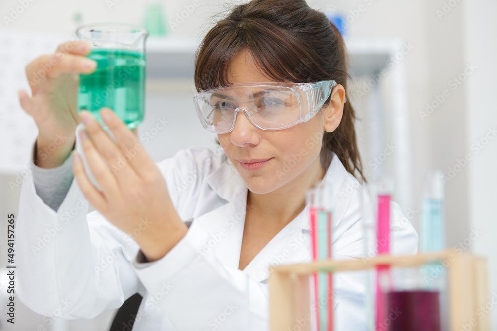 female scientist examining green liquid in beaker female scientist examining green liquid in beaker