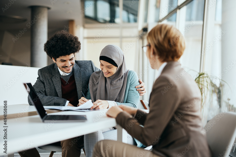 Happy Middle Eastern couple signs an agreement with insurance agent in the office. Happy Middle Eastern couple signs an agreement with insurance agent in the office.