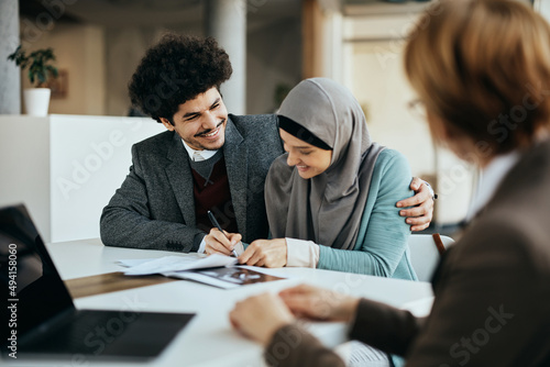 Young happy Muslim couple signs contract with real estate argent during meeting in the office.