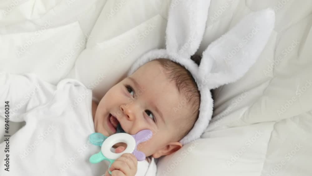 cute little boy , baby, toddler, sitting on white blanket with white bunny easter ears and chewing a soft teething toy. adorable photography for easter holidays. rubber toy for child’s teeth. cute little boy , baby, toddler, sitting on white blanket with white bunny easter ears and chewing a soft teething toy. adorable photography for easter holidays. rubber toy for child’s teeth.