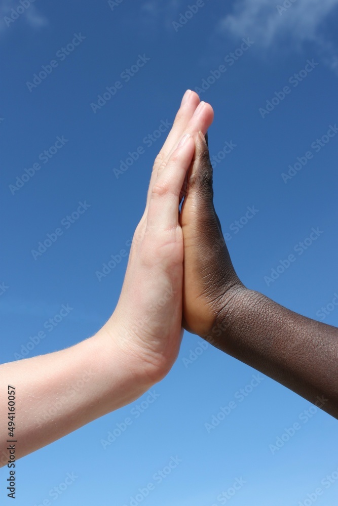 a white-skinned hand and a black-skinned hand high-five each other in front of a blue sky a white-skinned hand and a black-skinned hand high-five each other in front of a blue sky
