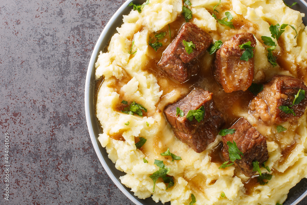 Slowly stewed beef with wine and vinegar garnished with mashed potatoes close-up in a plate on the table. horizontal top view from above Slowly stewed beef with wine and vinegar garnished with mashed potatoes close-up in a plate on the table. horizontal top view from above