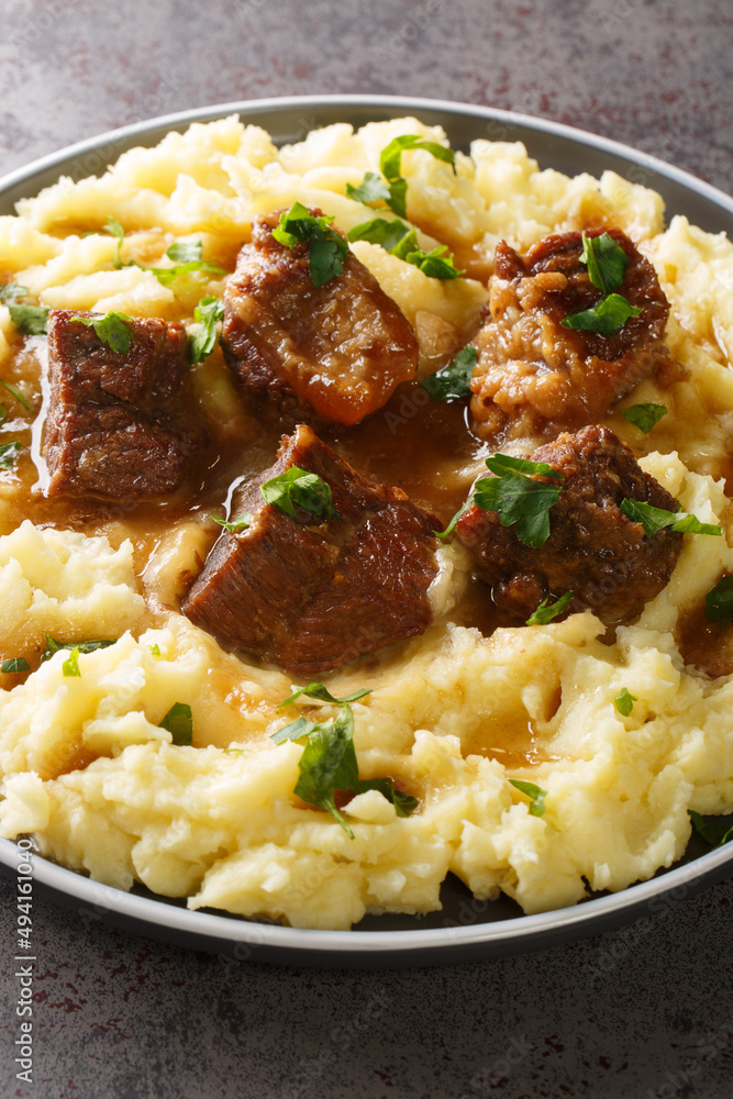 Greek sofrito is a dish consisting of tender cuts of beef slowly sauteed in a flavorful sauce served with mashed potatoes closeup in the plate on the table. Vertical