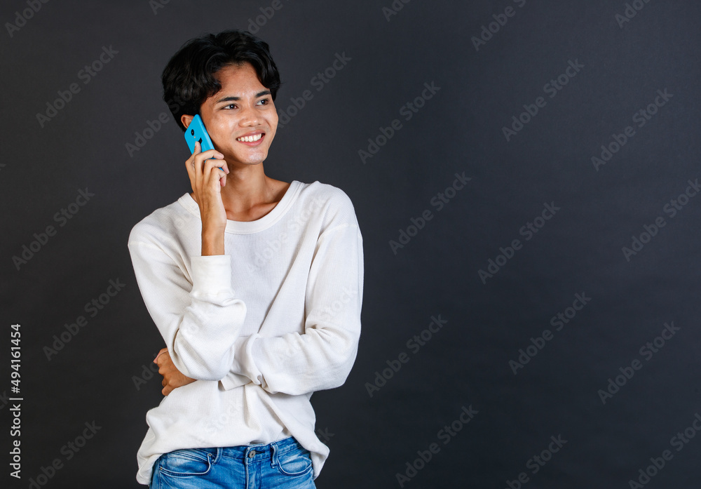 Fototapeta premium Studio shot of Asian young LGBTQ gay glamour handsome bisexual homosexual male model in casual outfit standing smiling holding smartphone on black background