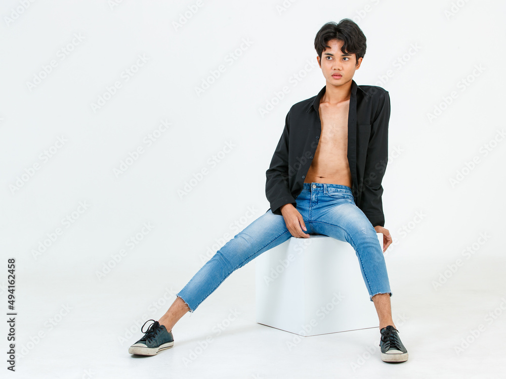 Portrait studio shot of Asian young LGBT gay bisexual homosexual topless male fashionable model in casual black shirt and denim jeans sitting on square boxes posing look at camera on white background Portrait studio shot of Asian young LGBT gay bisexual homosexual topless male fashionable model in casual black shirt and denim jeans sitting on square boxes posing look at camera on white background