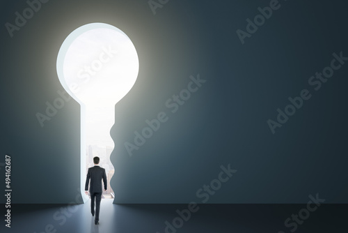 Back view of businessman standing in abstract key opening in wall with bright light and mock up place. Solution and decision concept.