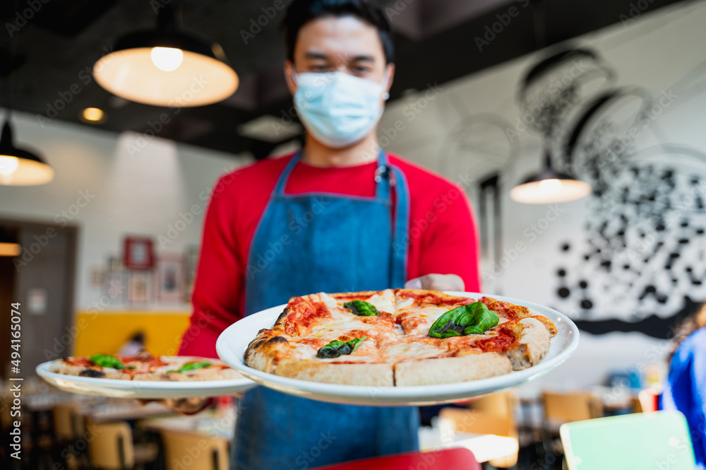 Unrecognizable waiter with face mask serving Italian pizza margherita.