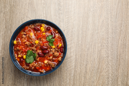 Bowl with tasty chili con carne on wooden table, top view. Space for text