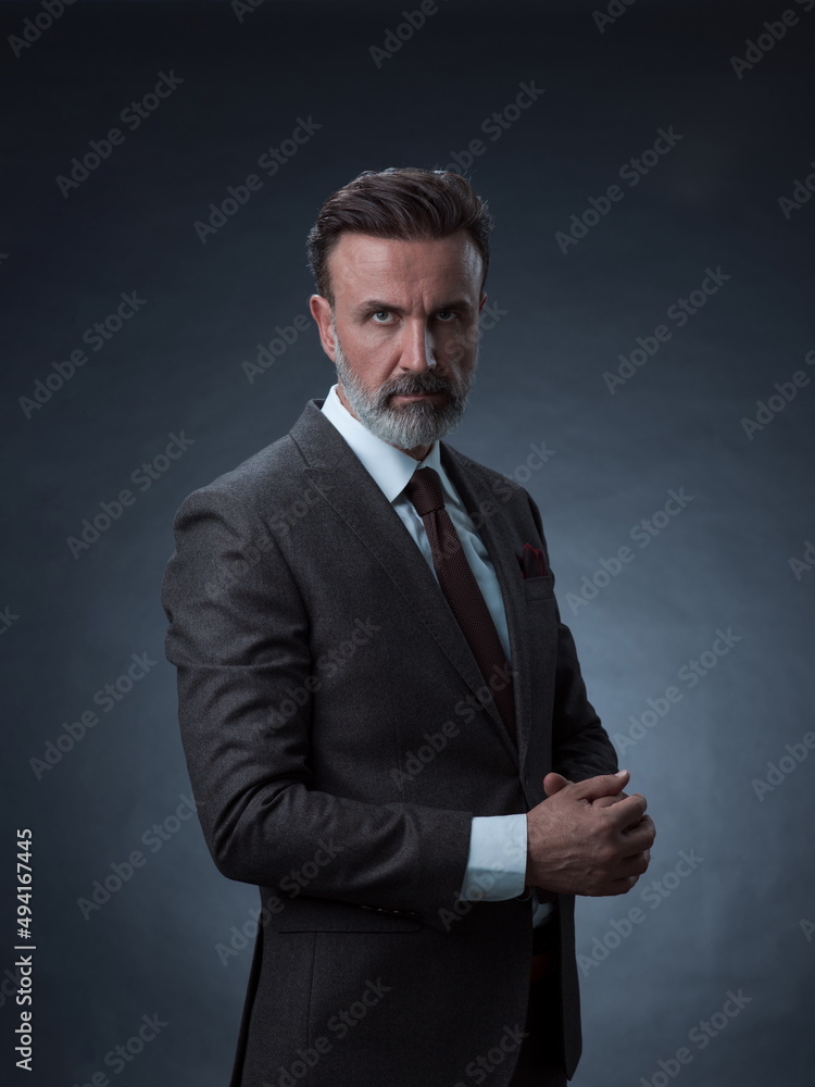 Portrait of a stylish elegant senior businessman with a beard and casual business clothes in photo studio isolated on dark background gesturing with hands Portrait of a stylish elegant senior businessman with a beard and casual business clothes in photo studio isolated on dark background gesturing with hands