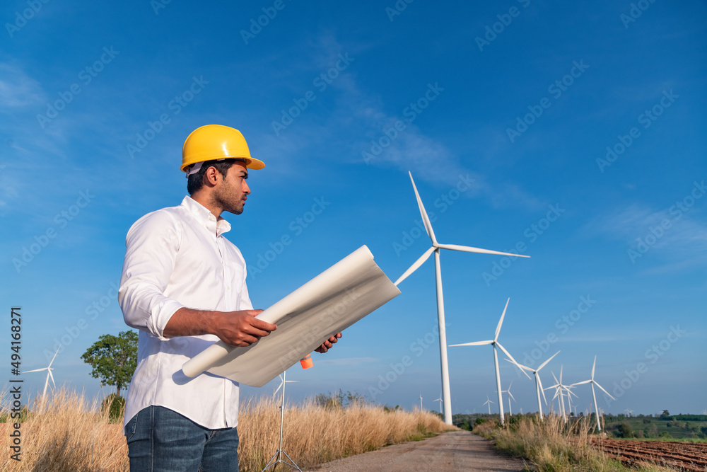 Engineer wearing uniform ,helmet hold document inspection work in wind turbine farms rotation to generate electricity energy. Green ecological power energy generation wind sustainable energy concept. Engineer wearing uniform ,helmet hold document inspection work in wind turbine farms rotation to generate electricity energy. Green ecological power energy generation wind sustainable energy concept.