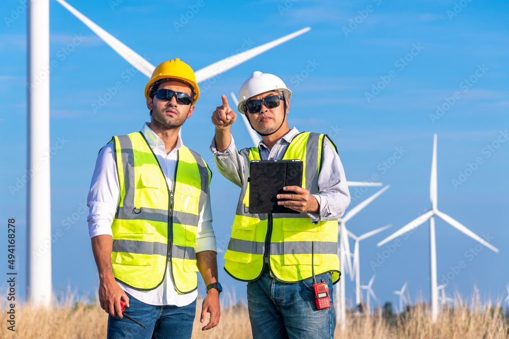 Engineer wearing uniform ,helmet hold document inspection work in wind turbine farms rotation to generate electricity energy. Green ecological power energy generation wind sustainable energy concept. Engineer wearing uniform ,helmet hold document inspection work in wind turbine farms rotation to generate electricity energy. Green ecological power energy generation wind sustainable energy concept.