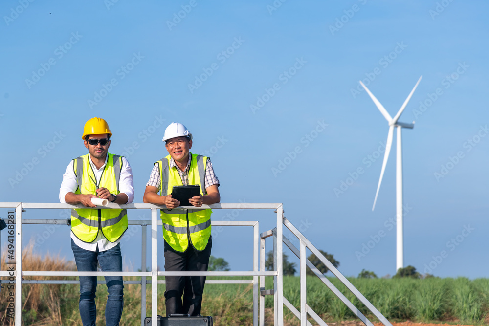Engineer wearing uniform ,helmet hold document inspection work in wind turbine farms rotation to generate electricity energy. Green ecological power energy generation wind sustainable energy concept. Engineer wearing uniform ,helmet hold document inspection work in wind turbine farms rotation to generate electricity energy. Green ecological power energy generation wind sustainable energy concept.