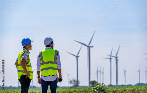Engineer wearing uniform ,helmet hold document inspection work in wind turbine farms rotation to generate electricity energy. Green ecological power energy generation wind sustainable energy concept.