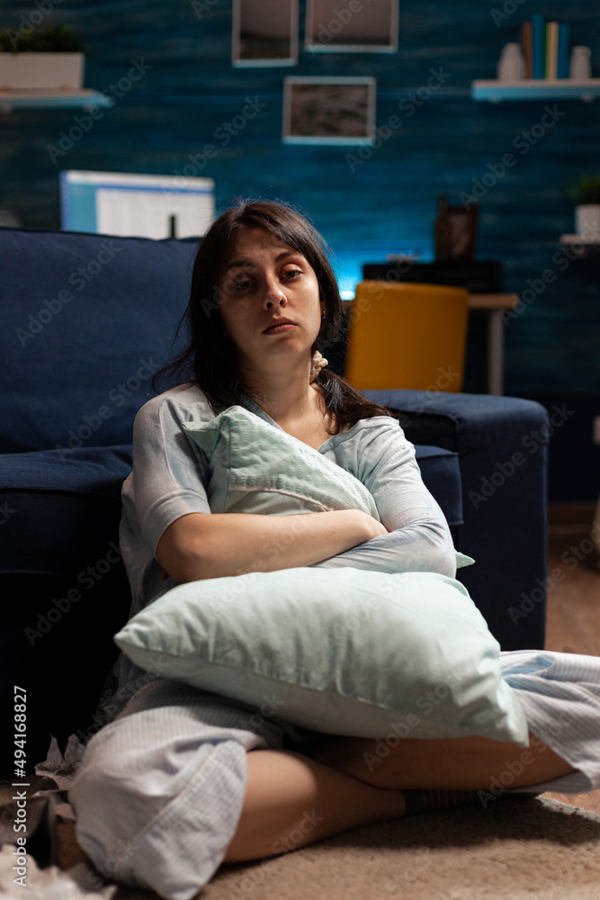 Portrait of depressed woman with mental health problems sitting on floor and hugging pillow in living room. Anxious sad person dealing with chronic disease difficulties and depression at home. Portrait of depressed woman with mental health problems sitting on floor and hugging pillow in living room. Anxious sad person dealing with chronic disease difficulties and depression at home.