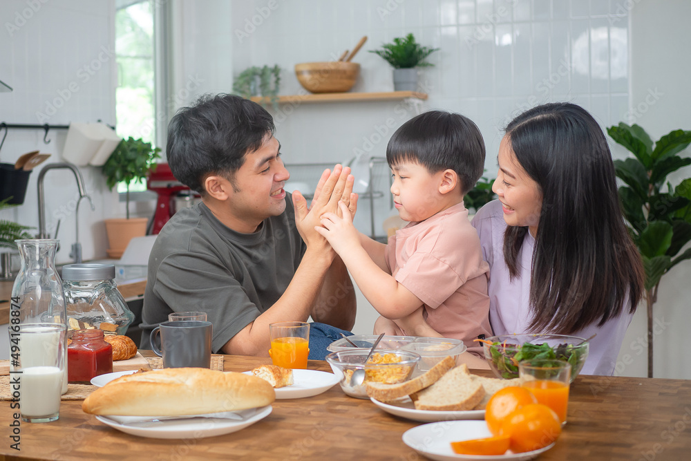 Asian family breakfast at happy home. Parents and children enjoy eating together, talking with laughter and good atmosphere. Father plays with son playfully at kitchen table Asian family breakfast at happy home. Parents and children enjoy eating together, talking with laughter and good atmosphere. Father plays with son playfully at kitchen table