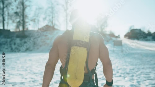 A bodybuilder without a T-shirt and in a hat with a drager balloon on his back walks through the snow to the hill. Back view. slow motion photo