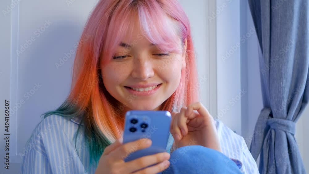 Happy Ukrainian girl browsing internet on mobile phone and laughing. Cute white female with dyed rainbow hair using modern smartphone with cheerful smile Happy Ukrainian girl browsing internet on mobile phone and laughing. Cute white female with dyed rainbow hair using modern smartphone with cheerful smile
