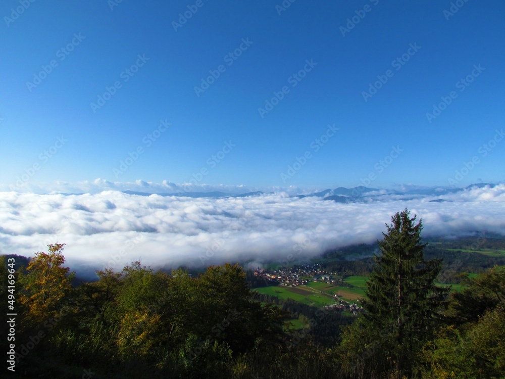 View of Gorenjska region of Slovenia covered in white fluffy clouds with hills in the back and the village of Preddvor bellow the mountains