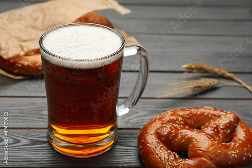 Mug of beer with tasty freshly baked pretzel on grey wooden table  closeup