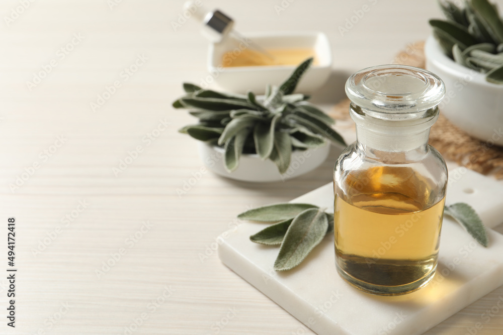 Bottle of essential sage oil and leaves on white wooden table. Space for text Bottle of essential sage oil and leaves on white wooden table. Space for text