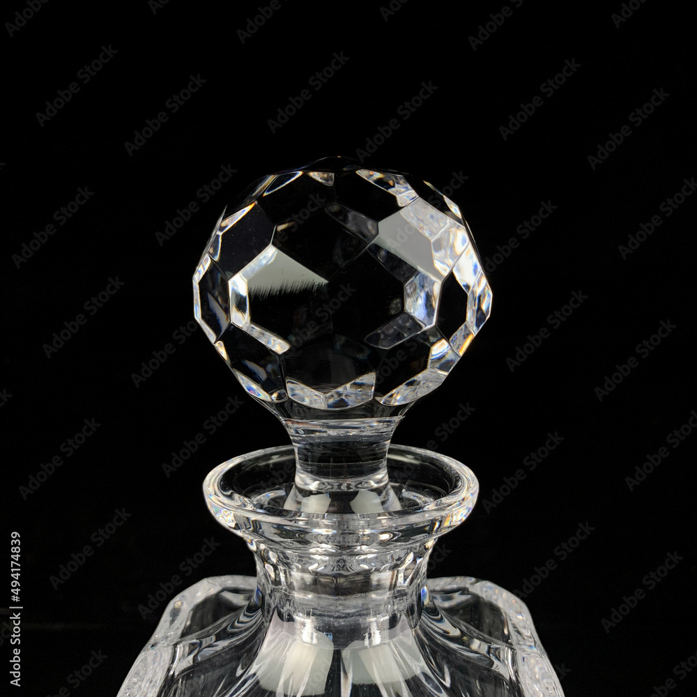 antique glass decanter with geometric pattern. glass faceted lid from gcarafe close-up on a black isolated background antique glass decanter with geometric pattern. glass faceted lid from gcarafe close-up on a black isolated background