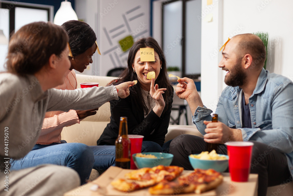 Man and women enjoying guessing game with sticky notes, playing charades together at drinks celebration after work hours. Office workmates having fun with patnomime activity at party. Man and women enjoying guessing game with sticky notes, playing charades together at drinks celebration after work hours. Office workmates having fun with patnomime activity at party.