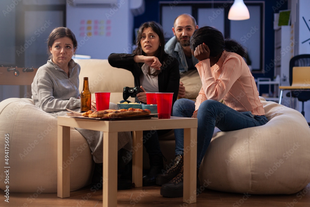 Coworkers feeling frustrated about lost video games play, doing leisure activity at office party after hours. Sad colleagues having fun with technology, beer bottles and pizza at celebration.