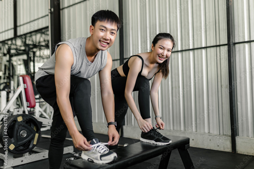 Obraz premium exercise concept The man and woman in the sport club resting one of their feet on the black bench and trying to tie up their shoelace