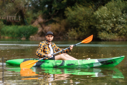 Handsome bearded caucasian man in shirt and cap kayaking at the river. The concept of water sport and activities
