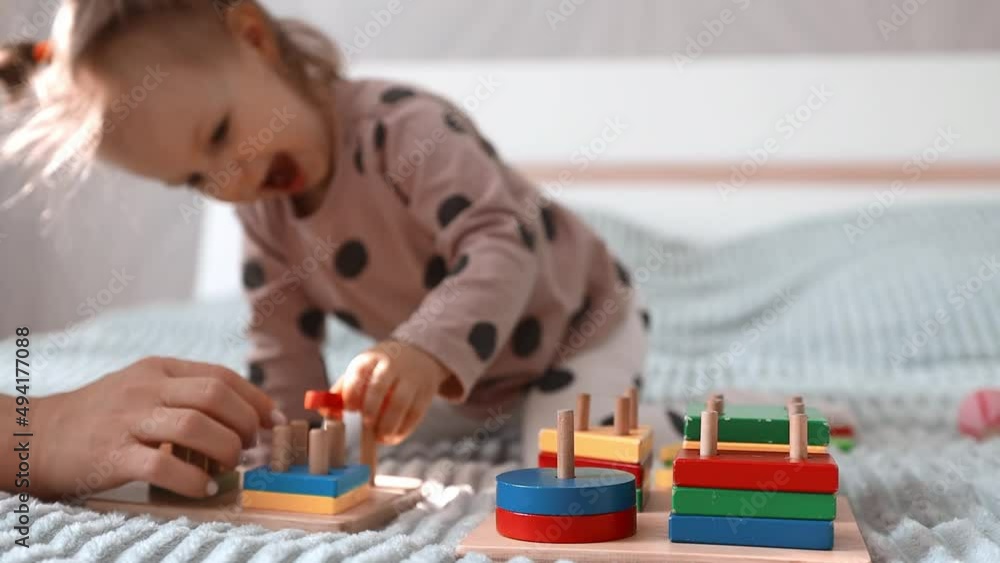 The child plays with wooden learning blocks while sitting on the bed. A little girl has fun playing logic games and learning. The child plays with wooden learning blocks while sitting on the bed. A little girl has fun playing logic games and learning.