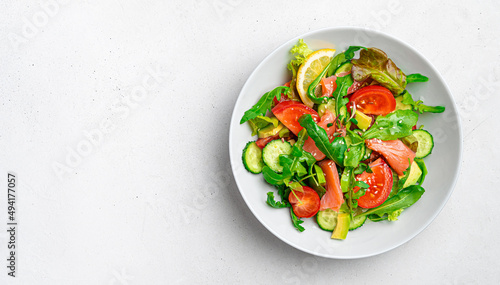 Salad with salmon, vegetables and fresh herbs on a light background.