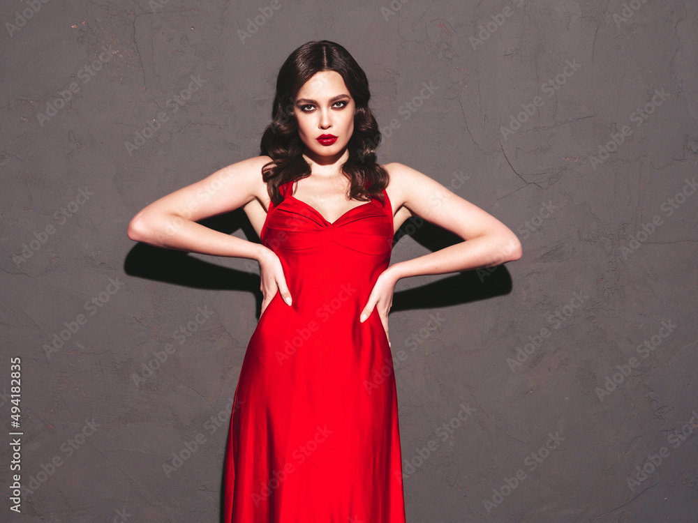 Beauty portrait of young brunette woman with evening makeup and perfect clean skin. Sexy model with curly hair posing in studio. With red bright natural lips.Posing near grey wall. In fashion dress Beauty portrait of young brunette woman with evening makeup and perfect clean skin. Sexy model with curly hair posing in studio. With red bright natural lips.Posing near grey wall. In fashion dress