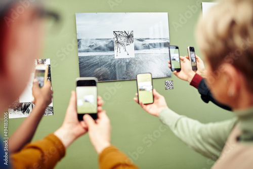 Unrecognizable people scanning QR code using smartphones to get more information about photo on wall at exhibition photo