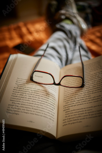 Libro abierto en el regazo con gafas sobre la cama