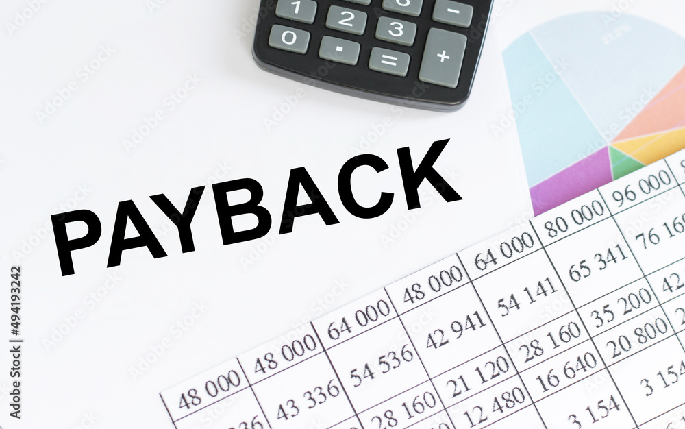 Text PAYBACK on notepad on the table next to reports and graphs, calculator Text PAYBACK on notepad on the table next to reports and graphs, calculator