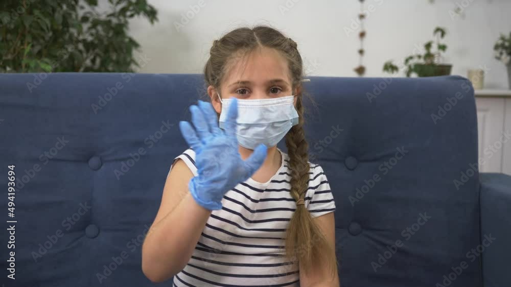 Child in safety mask waves his hand to camera. child uses medical mask. latex gloves for health safety. Child at home in quarantine sends hello hello laptop camera. Technology at distance Child in safety mask waves his hand to camera. child uses medical mask. latex gloves for health safety. Child at home in quarantine sends hello hello laptop camera. Technology at distance